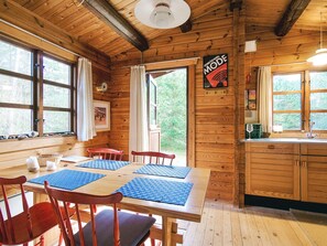A wooden cabin with a dining area featuring a table and chairs, a kitchen with a sink and cabinets, and large windows offering views of the surrounding forest. - 4 Person Holiday Home in Store Fuglede (Store Fuglede)