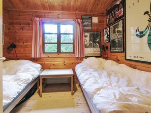 Cozy cabin-style room with two single beds, a wooden bench, and a window with curtains.
