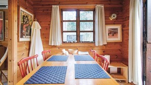 Une cabane en bois avec une grande table à manger, des chaises rouges et une fenêtre avec des rideaux.