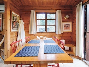 Una cabaña de madera con una gran mesa de comedor, sillas rojas y una ventana con cortinas.