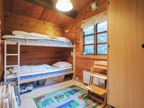 A wooden cabin room with bunk beds, a window, a radiator, and a small wooden chair.
