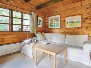 A cozy cabin interior with a wooden ceiling, a white sofa, a small wooden table, and framed pictures on the walls.