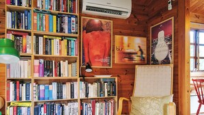 Une pièce chaleureuse aux murs en bois, avec une bibliothèque remplie de livres, un fauteuil confortable et un panier posé sur le sol.