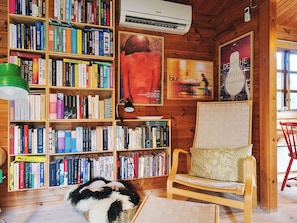 Una habitación acogedora con paredes de madera, una estantería llena de libros, un sillón cómodo y una cesta en el suelo.