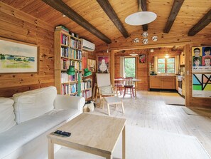 A cozy cabin interior with a wooden interior, a white sofa, a dining table with chairs, a bookshelf, and a kitchen area. - 4 Person Holiday Home in Store Fuglede (Store Fuglede)