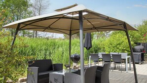 Une terrasse extérieure dotée d’un espace salon couvert, d’un barbecue et d’une table avec des chaises.