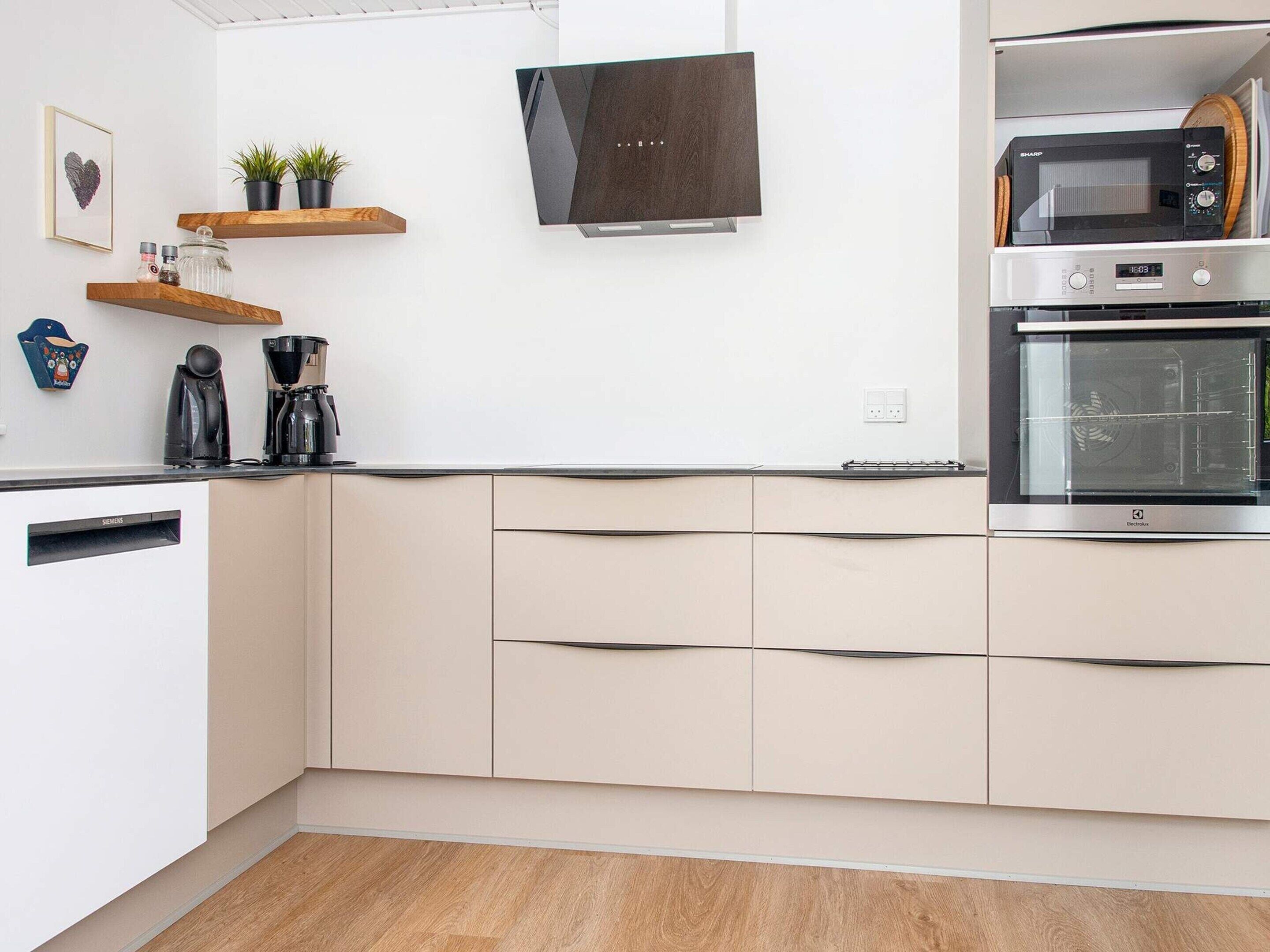 Eine moderne Küche mit Geschirrspüler, Backofen und Mikrowelle. Holzregale mit Pflanzen und Gewürzen, ein Kaffeeautomat auf der Arbeitsplatte.