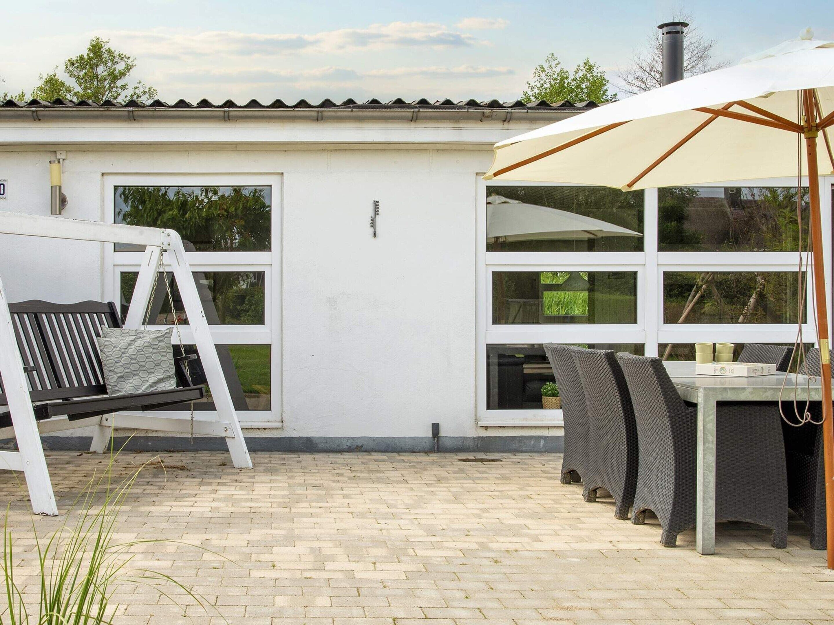 Une terrasse avec une balançoire, une table avec des chaises et un grand parasol.