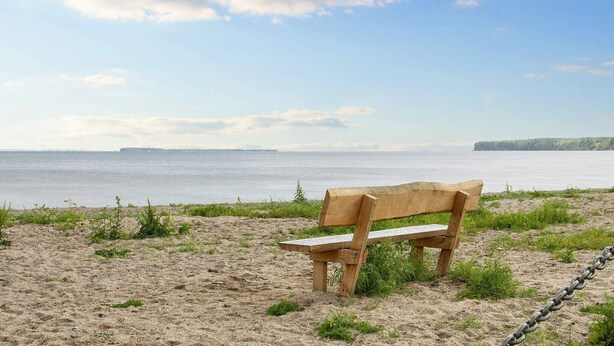 Un banc en bois sur une plage de sable, avec vue sur la mer et une étendue de terre lointaine.