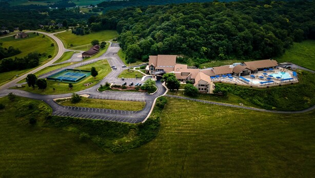 An aerial view of a resort with a swimming pool, tennis courts, and a large building surrounded by greenery. - Valleywood Villa (Galena)