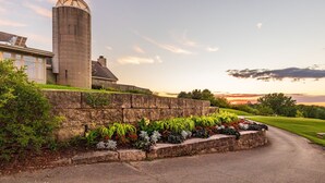 A large building with a cylindrical tower, a stone retaining wall with a flower bed, and a well-maintained lawn. - Valleywood Villa (Galena)
