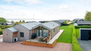 Een modern huis met een ruim terras, een overdekte zithoek en uitzicht op het water.