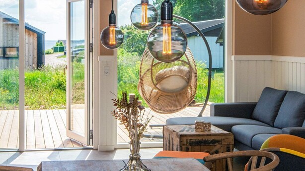 Een moderne woonkamer met een grote glazen deur die uitkomt op een terras, rieten meubels en hanglampen.