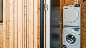 Een kleine wasruimte met een voorlader wasmachine en droger, houten wanden en een klein raam.