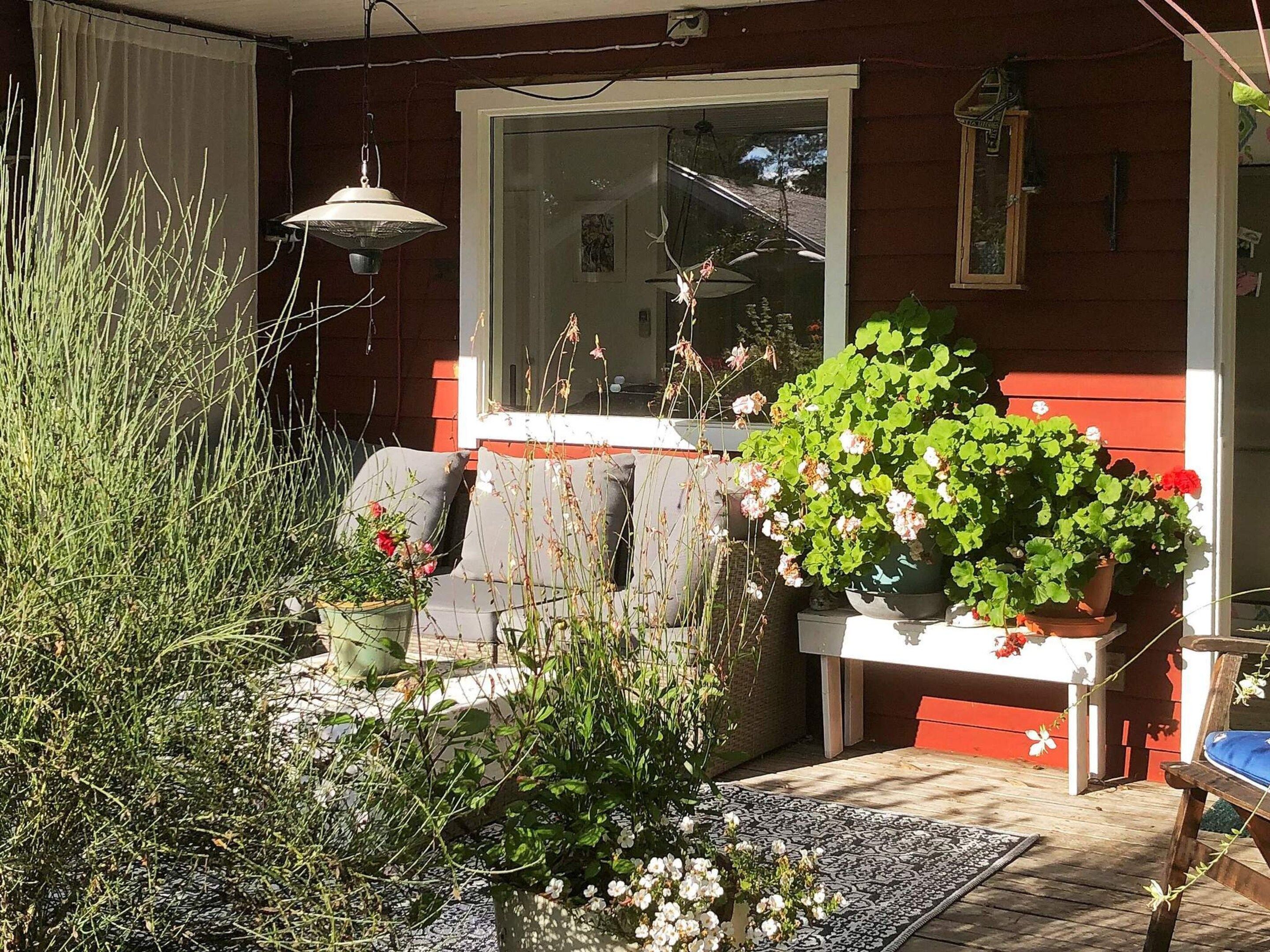 Uma casa vermelha com varanda, uma janela e várias plantas.