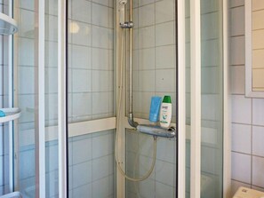 Lasiseinöillä varustettu suihku, jossa on käsisuihkupää ja erillinen käsisuihkun letku. Seinällä on kaksi pulloa shampoota ja hoitoainetta.