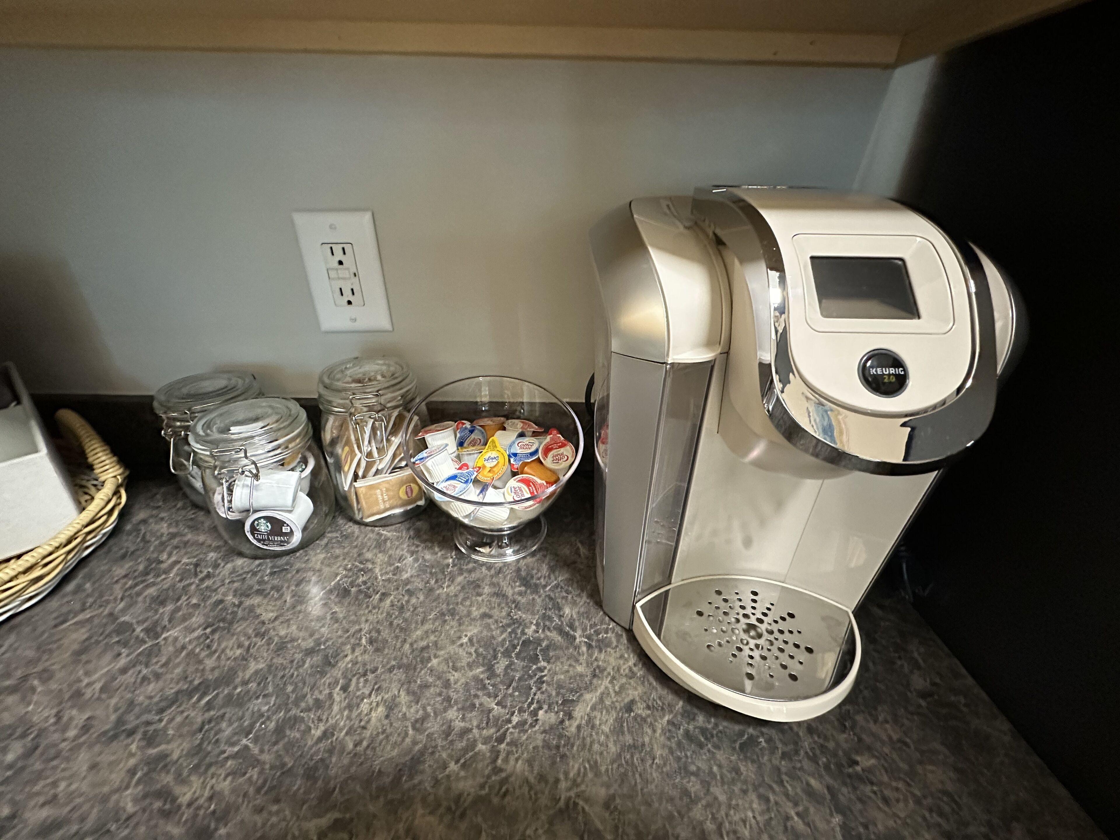 A coffee maker, a bowl of coffee pods, and two glass jars on a kitchen counter.