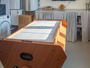 Ein Zimmer mit einem Kicker, einer Waschmaschine und einem Tisch mit gemusterten Vorhängen.