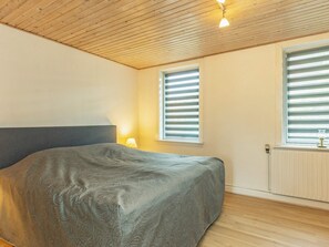 A bedroom with a bed, a window with blinds, a radiator, and a ceiling with wooden beams. - 10 Person Holiday Home in Vestervig (Vestervig)