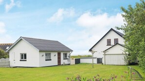 A two-story white house with a sloped roof, a fenced yard, and a garden with purple flowers. - 10 Person Holiday Home in Vestervig (Vestervig)