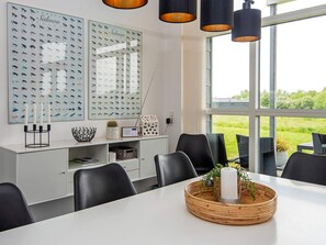 A modern dining area with a white table, black chairs, and a large window offering a view of greenery.