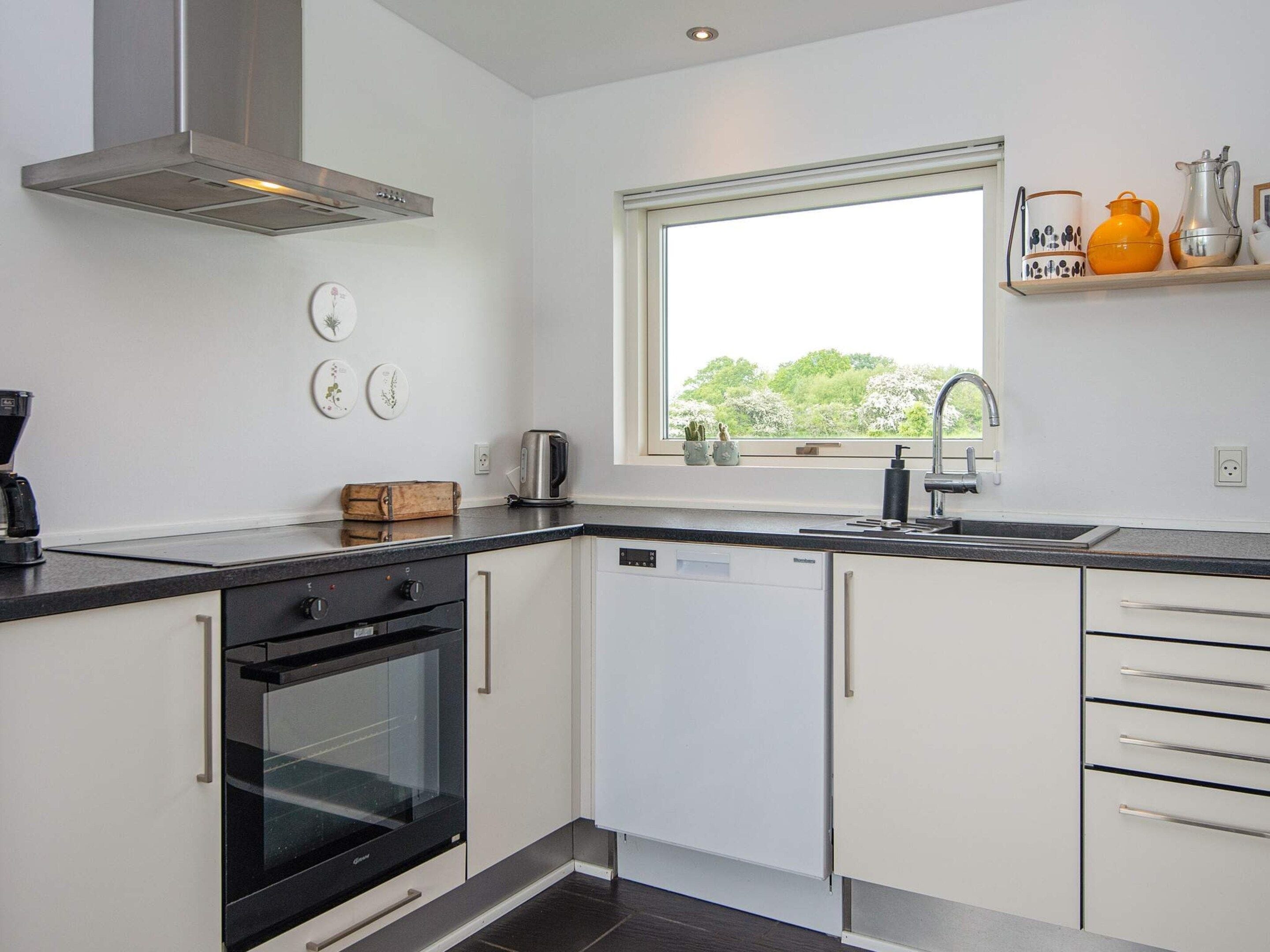 A modern kitchen with a dishwasher, oven, and a window with a view of greenery.