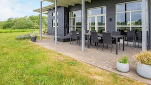 Un espace extérieur moderne, aménagé avec un patio couvert, de grandes fenêtres et des plantes en pot.