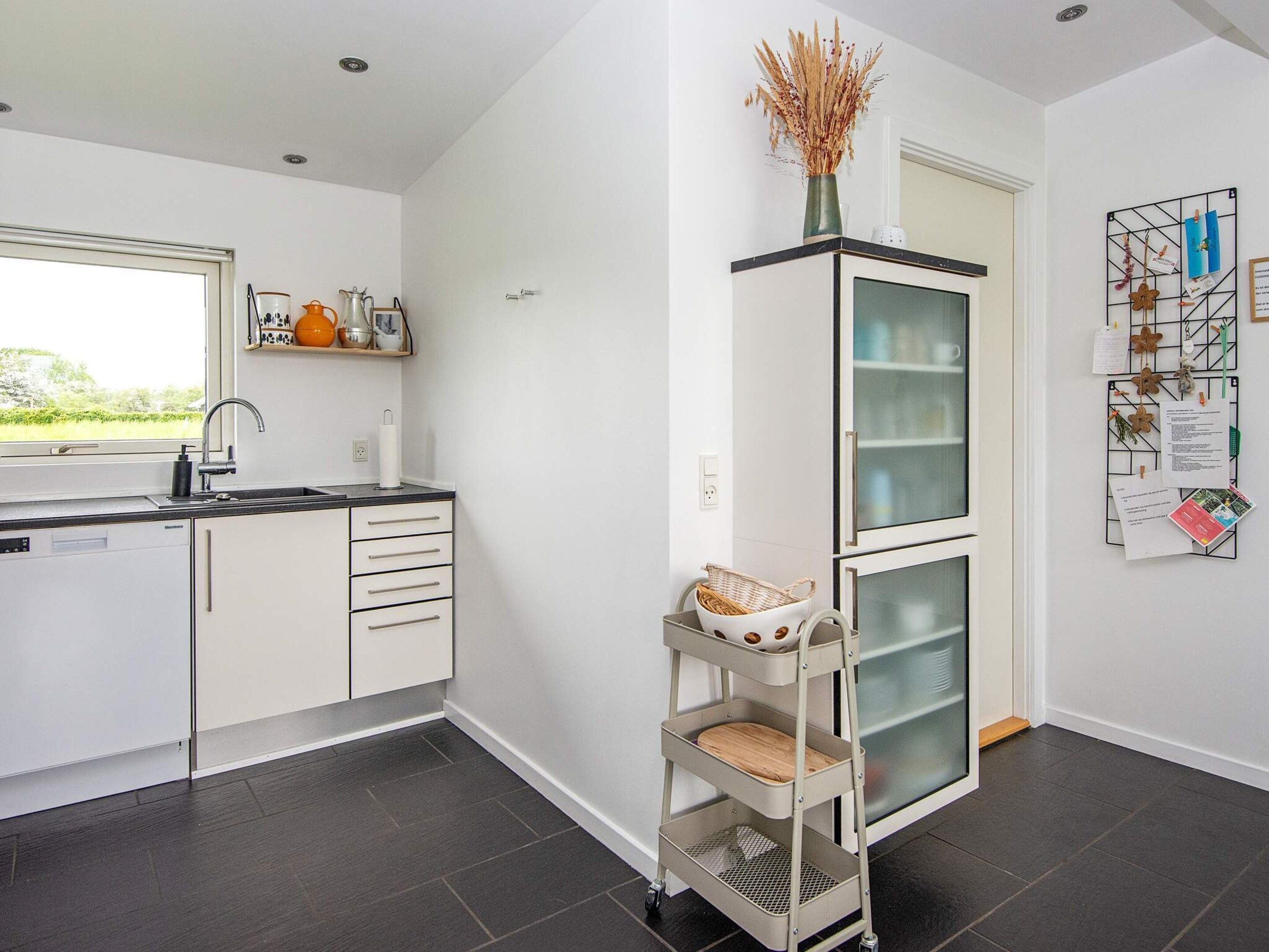 A modern kitchen with a built-in dishwasher, a window with a view, and a wall-mounted rack with papers and decorations.