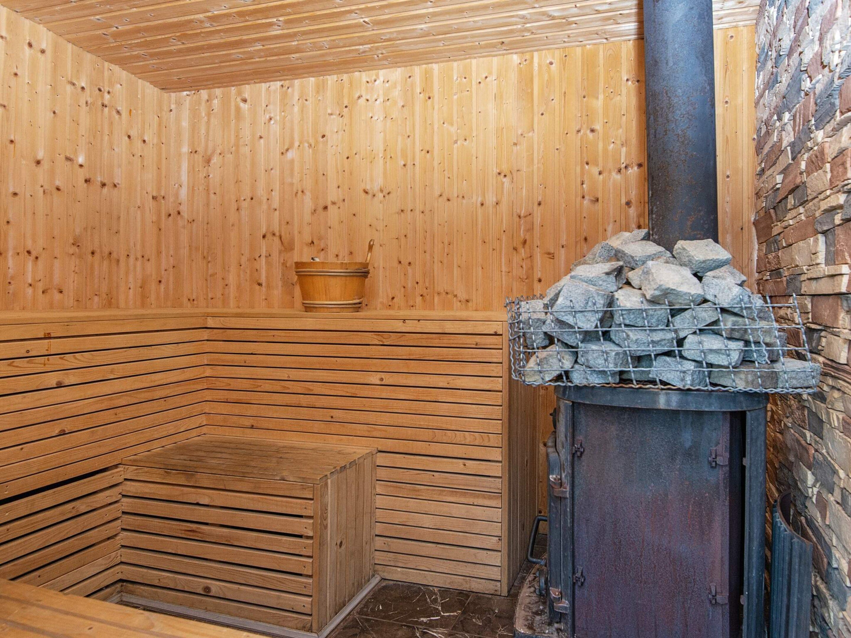 A sauna with wooden walls, a bench, a stone wall, and a metal stove.
