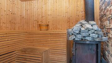 A sauna with wooden walls, a bench, a stone wall, and a metal stove.