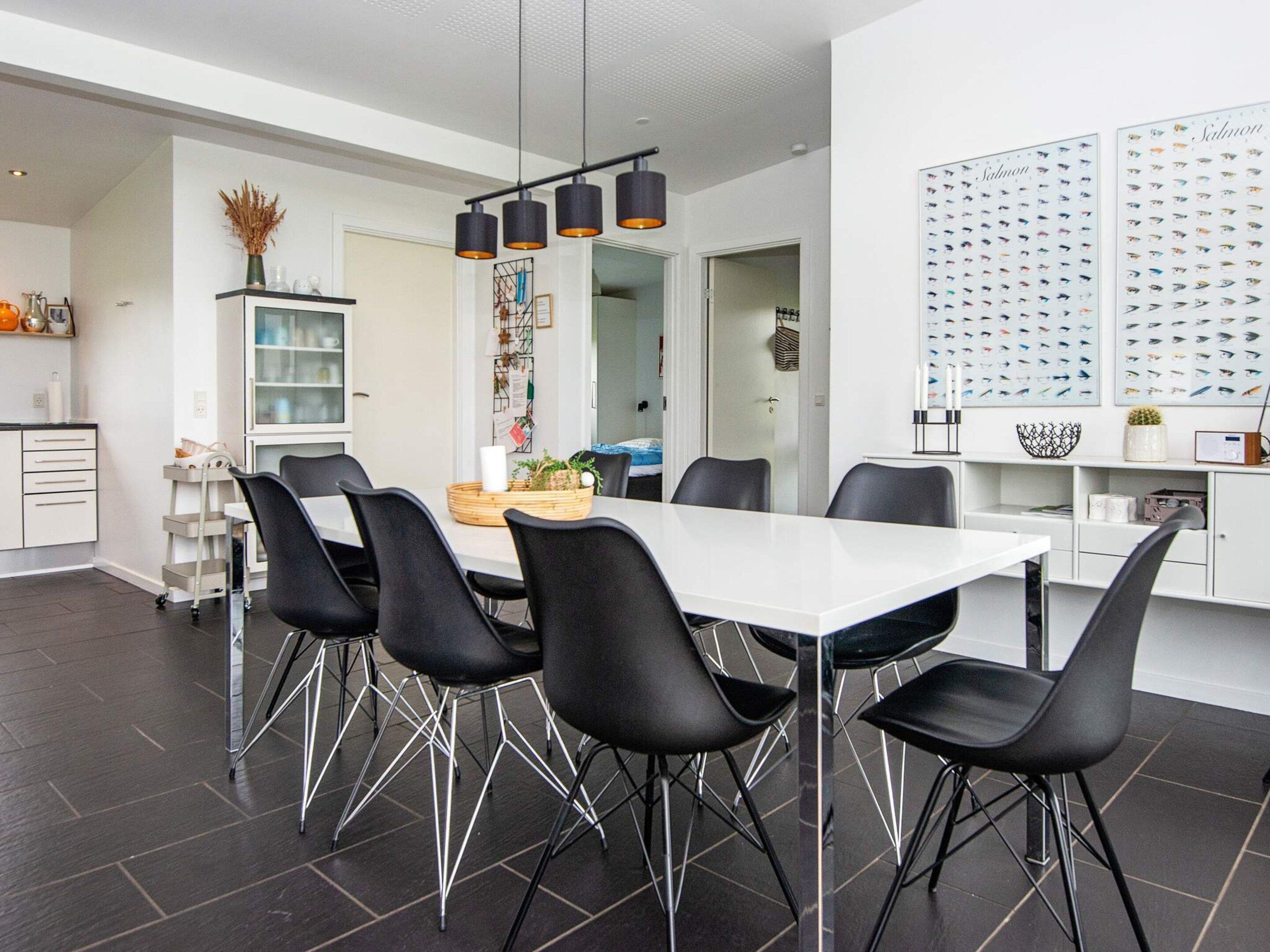 A modern dining area with a white table, black chairs, and pendant lighting.