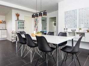 Un comedor moderno con una mesa blanca, sillas negras e iluminación colgante.