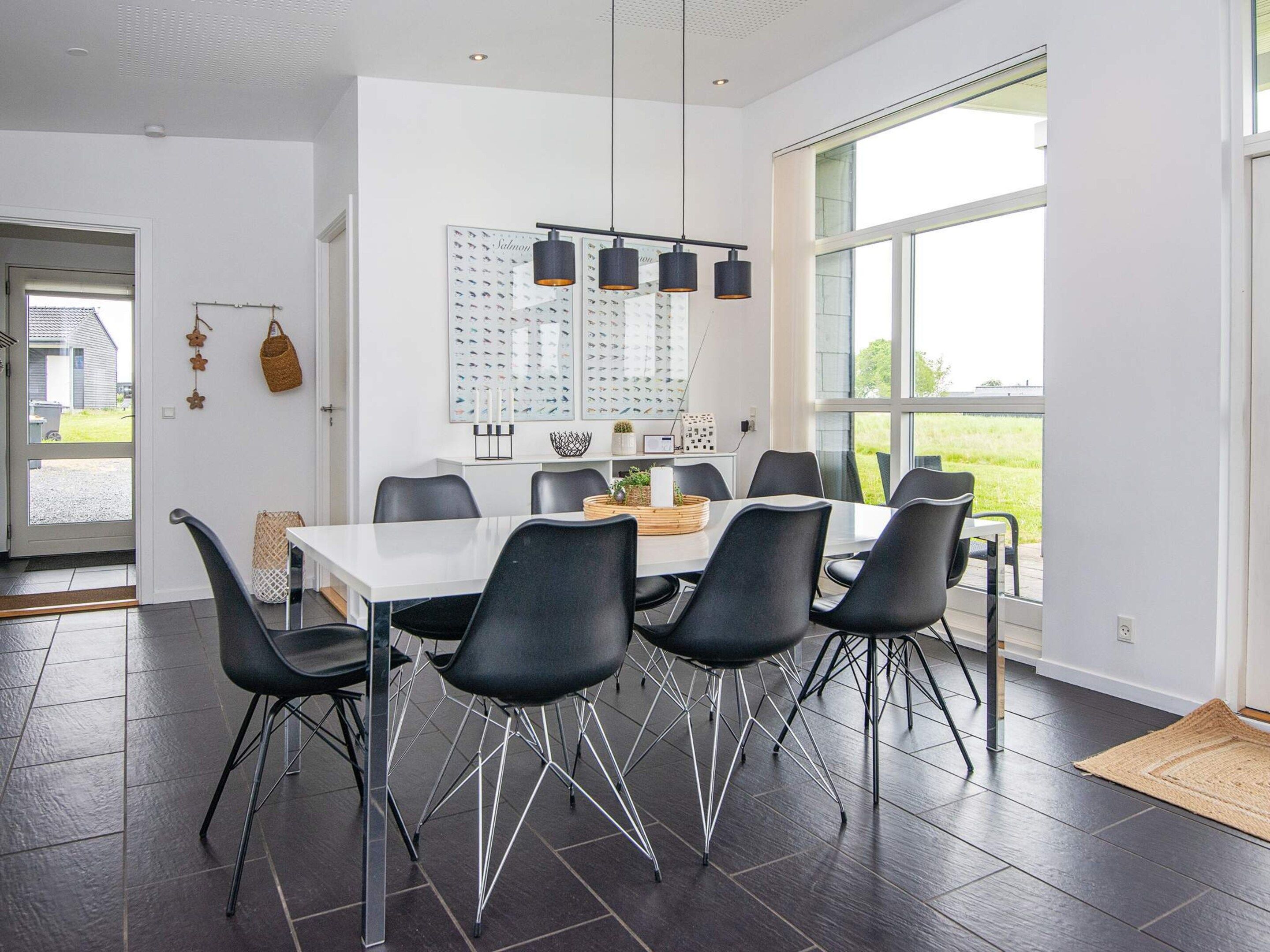 A modern dining area with a white table, black chairs, and pendant lighting.