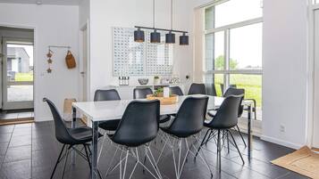 A modern dining area with a white table, black chairs, and pendant lighting.