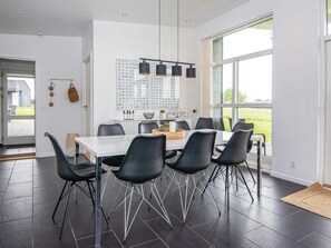 Uma área de refeições moderna com mesa branca, cadeiras pretas e iluminação pendente.