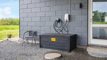 A black storage box with a yellow label, a chair, and a wall-mounted power outlet with a cable.