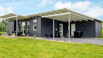A modern building with a covered patio area, large windows, and a grassy lawn.