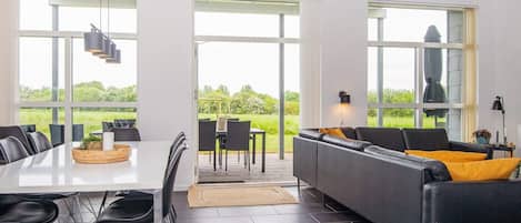 A modern living room with a dining area, large windows, and a view of greenery.