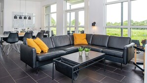 Un salon moderne avec un canapé en cuir noir, une table basse et de grandes fenêtres donnant sur l’extérieur.