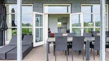 An outdoor dining area with a table and chairs, a covered seating area, and a view of the garden.
