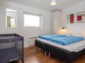 Un dormitorio con cama, ventana, radiador, banco y una lámpara de pared.