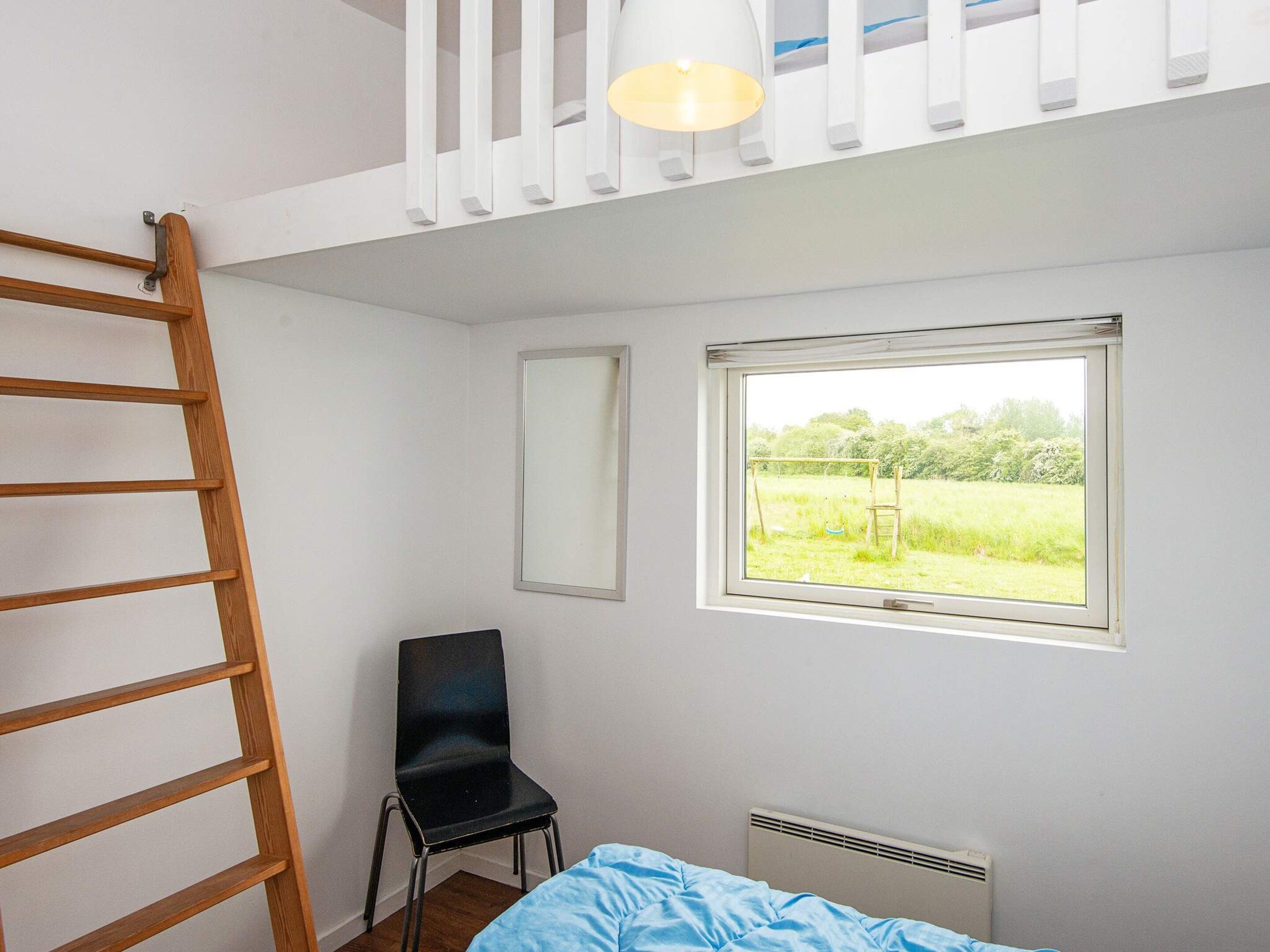 A bedroom with a bunk bed, a chair, a window with a view of a field, and a radiator.