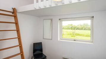 A bedroom with a bunk bed, a chair, a window with a view of a field, and a radiator.