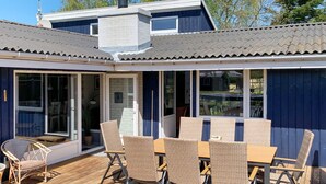 A covered outdoor deck with a table and chairs, a potted plant, and a sliding glass door. - 8 Person Holiday Home in Vaeggerlose (Vaeggerlose)