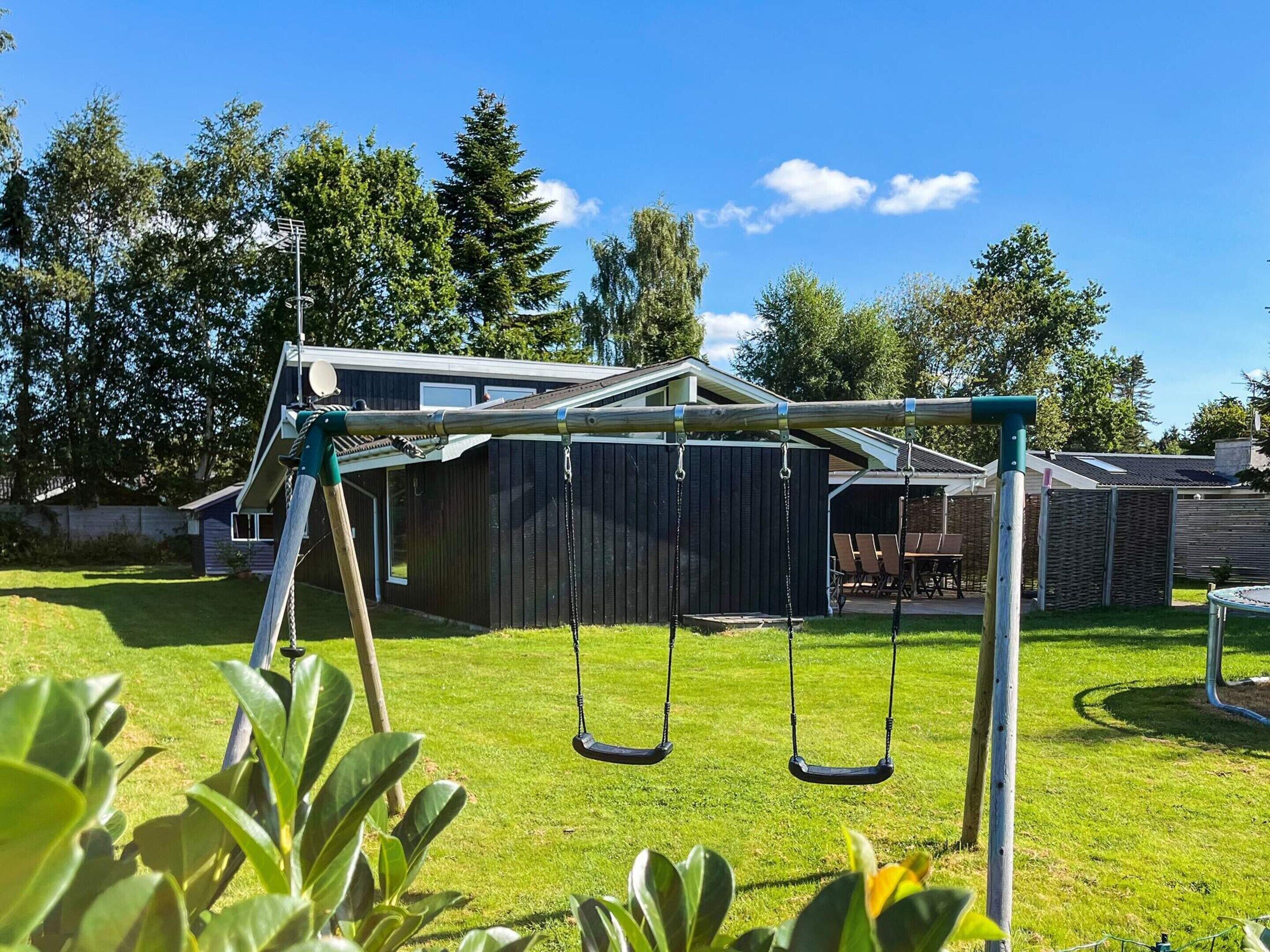 Ein Garten mit Schaukel, Holzschuppen und einem Haus im Hintergrund.