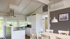 A modern kitchen with white cabinetry, a central island, and a dining area with white chairs. - 8 Person Holiday Home in Vaeggerlose (Vaeggerlose)