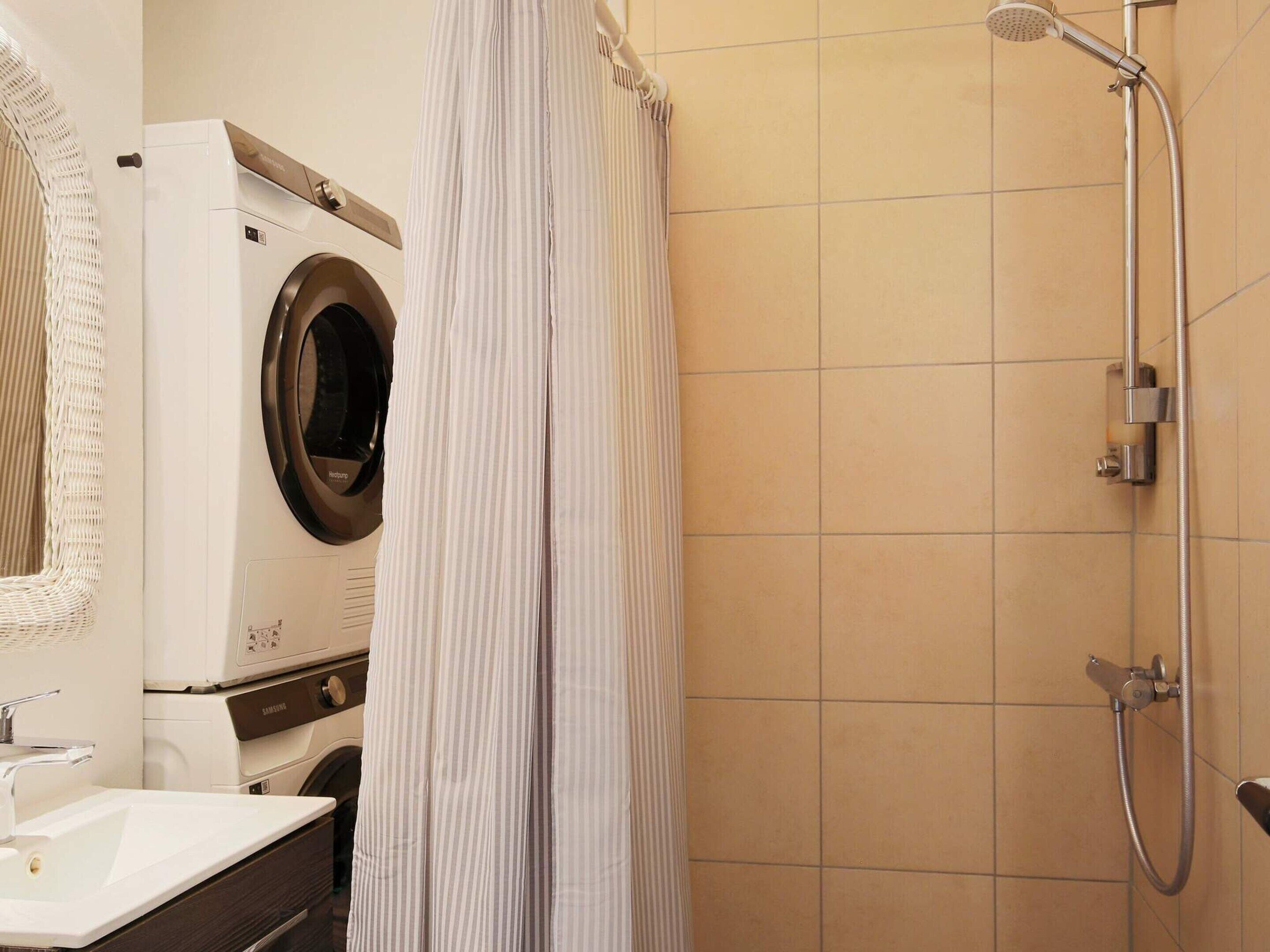 A bathroom with a washing machine, a shower, and a sink.