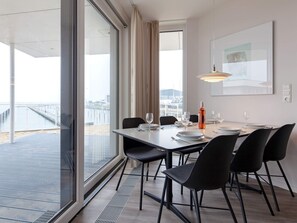 A dining area with a table set for four, large windows, and a view of a pier. - 5 Star Holiday Home in Wendtorf (Wendtorf)