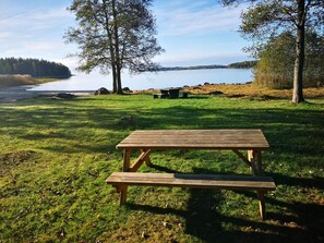 Ett picknickbord på en gräsyta med en sjö och träd i bakgrunden.