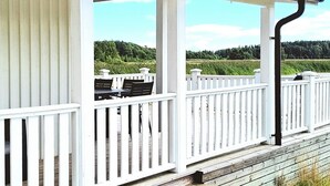 Una terraza cubierta al aire libre con barandas blancas, una mesa y sillas.